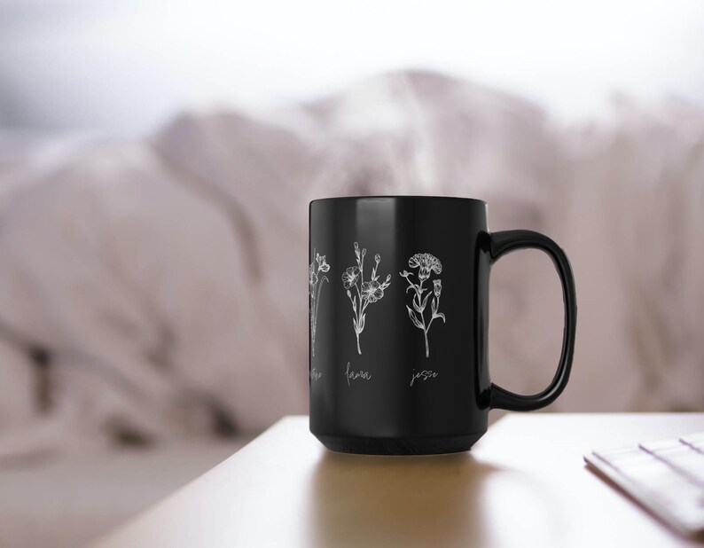 Puede incluir: Taza de caf&eacute; de cer&aacute;mica negra con un dise&ntilde;o floral blanco y los nombres "Jenna" y "Jesse" escritos debajo de las flores.