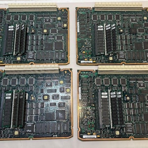May include: Four green circuit boards with various electronic components, including chips, connectors, and memory modules. The boards have a rectangular shape with a light brown border and a white connector at the top.