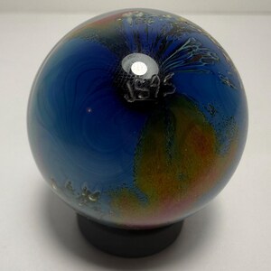 Puede incluir: Una esfera de vidrio decorativa con un patr&oacute;n arremolinado de tonos azules, naranjas y amarillos. La pieza de vidrio descansa sobre una base negra. El texto "JS45" est&aacute; grabado en el vidrio.