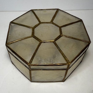 May include: An octagonal box constructed from translucent, off-white panels framed in thin, metallic brass-toned metal. The lid features a central hexagonal panel surrounded by eight trapezoidal panels, with matching panels forming the sides.