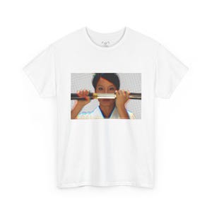 May include: White t-shirt featuring a graphic of a person holding a katana. The image has a glitch effect, with red and blue color distortions. The person is wearing a white top.