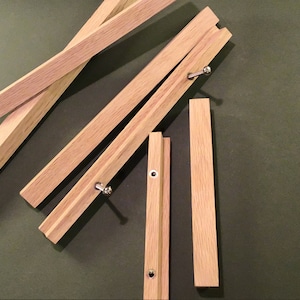 May include: Five wooden pieces of a folding easel, with metal hinges and screws. The pieces are arranged in a random pattern on a green surface.