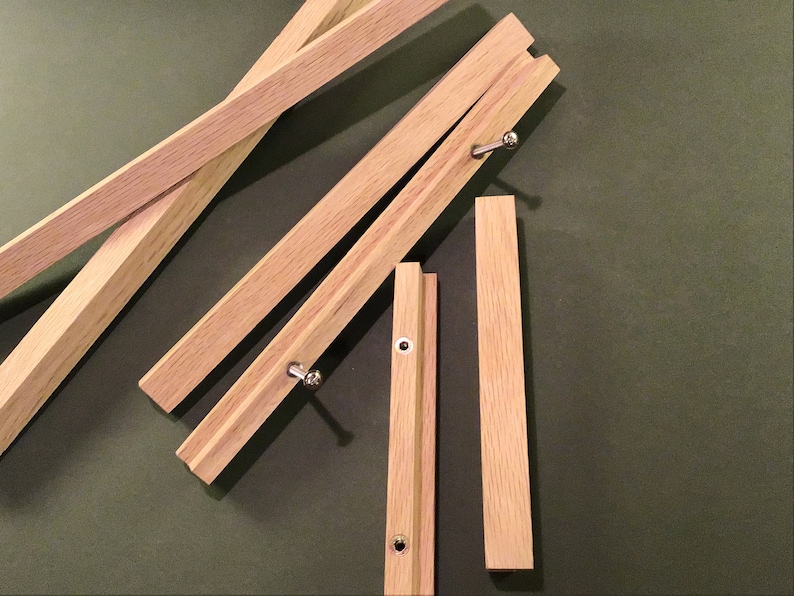 May include: Five wooden pieces of a folding easel, with metal hinges and screws. The pieces are arranged in a random pattern on a green surface.