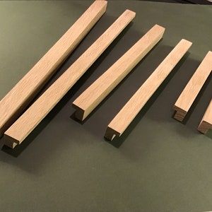 May include: Six wooden cabinet door pulls with a T-shaped design. The pulls are made of light brown wood and are arranged in a row on a green surface.