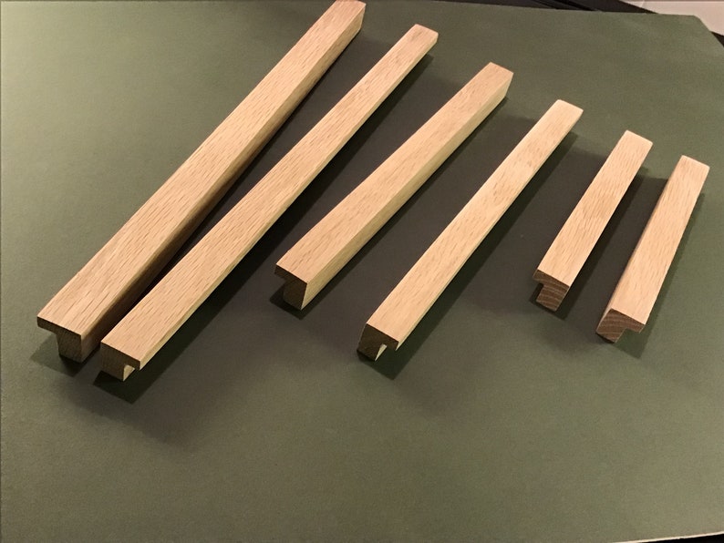 May include: Six wooden cabinet door pulls with a T-shaped design. The pulls are made of light brown wood and are arranged in a row on a green surface.