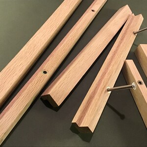 May include: Five pieces of unfinished, light brown wood with bevelled edges and screw holes. The wood pieces are arranged in a random pattern on a green surface.