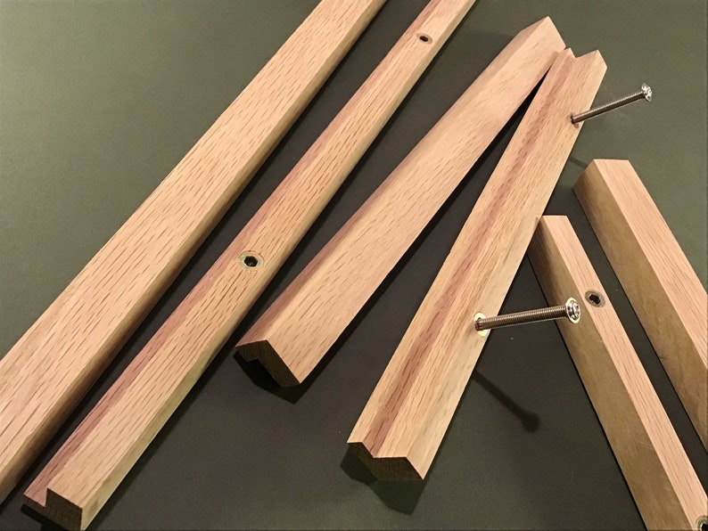May include: Five pieces of unfinished, light brown wood with bevelled edges and screw holes. The wood pieces are arranged in a random pattern on a green surface.