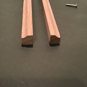 Peut inclure: Deux morceaux de moulure en bois non fini avec un bord décoratif. Un petit clou argenté est également visible.