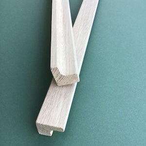 Peut inclure: Deux morceaux de moulure en bois non fini de couleur claire avec un bord décoratif. La moulure est disposée en forme de V.