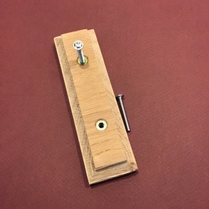 Peut inclure: Un bloc de bois avec deux trous de vis et une vis dans l'un des trous. Le bloc est sur une surface rouge.