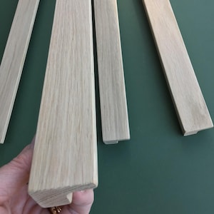 May include: Four pieces of unfinished, light wood trim with a bevelled edge. The trim is approximately 2.5 cm wide and 1.25 cm thick.