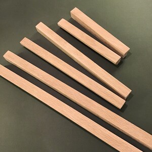 May include: Five wooden dowels of varying lengths, arranged in a fan shape on a green surface. The dowels are all the same width and have a natural wood finish.