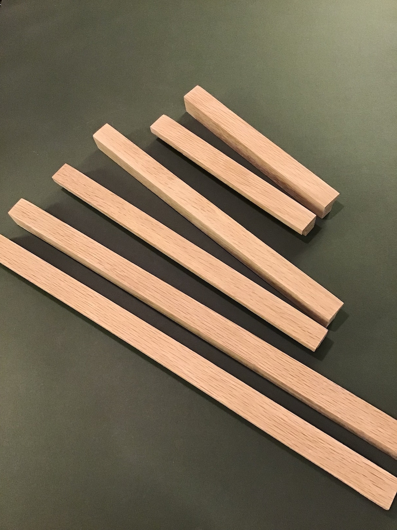 May include: Five wooden dowels of varying lengths, arranged in a fan shape on a green surface. The dowels are all the same width and have a natural wood finish.