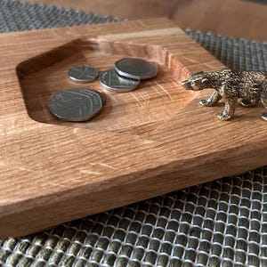 May include: A wooden tray with a recessed area containing several coins. A small, detailed bronze bear figurine stands on the tray's edge. The tray has a natural wood grain finish and is square-shaped.