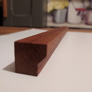 May include: A close-up of a dark brown wooden drawer pull with a bevelled edge.