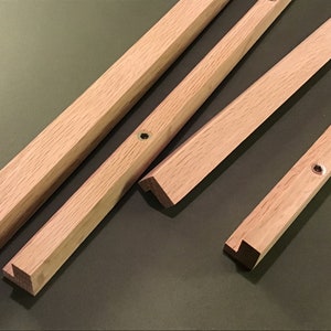 May include: Four wooden pieces with angled edges and a small hole drilled in each piece. The pieces are light brown in colour and appear to be part of a wooden frame.