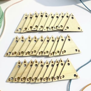 May include: A collection of light-coloured wooden triangular pieces arranged in three rows. The top row features pieces with small drilled holes and dot patterns. The middle row displays pieces marked with numbers 1, 2, and 3. The bottom row shows pieces labelled with letters A, B, and C.