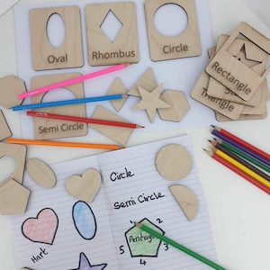 May include: A set of wooden shape stencils with labels for learning shapes. The shapes include a circle, oval, rhombus, semi-circle, rectangle, triangle, and star. The stencils are on a white surface with a notebook and coloured pencils.