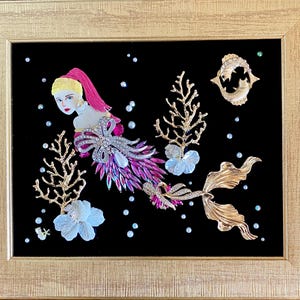 May include: A framed artwork featuring a mermaid design. The mermaid is crafted from jewelry pieces, with a pink and purple tail, a jeweled bow, and a blonde head with a pink ponytail. Gold coral and a fish brooch are also included.