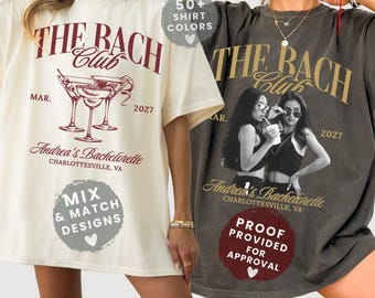 May include: Two oversized t-shirts, one ivory with a maroon graphic of martini glasses and text reading THE BACH CLUB MAR. 2027 Andrea's Bachelorette CHARLOTTESVILLE, VA, and one pepper grey with a photo graphic and gold text THE BACH CLUB.