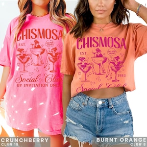 Two models in Comfort Colors brand shirt with graphic of Chismosa Social Club in color hot pink design and orange. Ovesized shirts in colors crunchberry & burnt Orange.