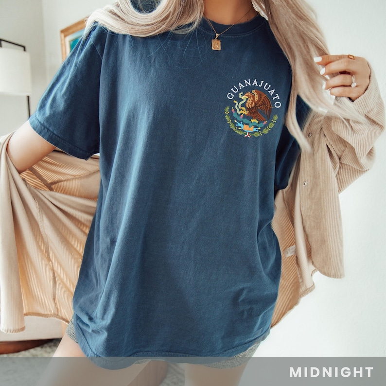 May include: A navy blue t-shirt with a white embroidered design of the coat of arms of Guanajuato, Mexico. The text "Guanajuato" is written in white above the design. The t-shirt is shown on a model wearing it. The color of the t-shirt is described as "Midnight".