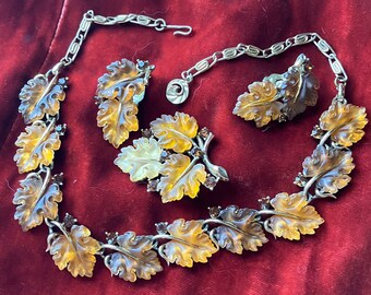 Op de afbeelding: Een gouden ketting en oorbellenset met gegraveerde amberen bladeren met heldere en bruine accenten. De ketting heeft een kettingschakelontwerp en de oorbellen zijn clip-on.