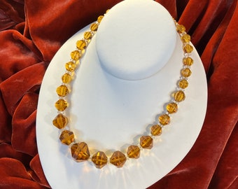 Peut inclure: Un collier composé de perles de verre facettées de couleur ambre. Le collier est présenté sur un buste de mannequin blanc sur un fond de velours rouge.