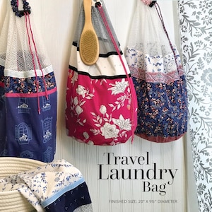 Op de afbeelding: Drie reistasjes voor wasgoed hangen aan haken. De tassen zijn gemaakt van gaas en stof met bloemenpatronen. De tas links is blauw met een wit raamontwerp. De middelste tas is roze met witte bloemen. De tas rechts is blauw met witte bloemen. De tekst "Travel Laundry Bag" staat onder de tassen. De tekst "FINISHED SIZE: 20" X 9 1/2" DIAMETER" staat onder de tekst "Travel Laundry Bag".