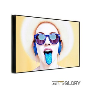 May include: A woman with a large, white afro wears blue sunglasses and headphones. Her tongue is sticking out and is covered in blue glitter.