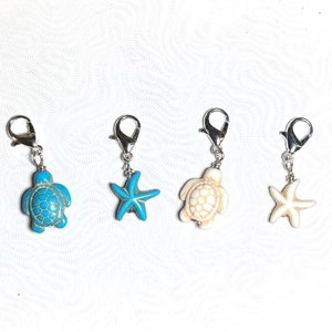 May include: Four silver charm clips with different sea-themed charms. Two charms are white turtle designs, one is a blue turtle design, and one is a white starfish design.
