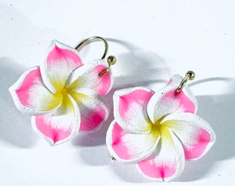 Puede incluir: Un par de pendientes con diseños de flores rosas y blancas con aros dorados.