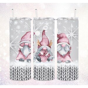 Peut inclure: Trois gobelets en acier inoxydable sur le thème des gnomes d'hiver. Chaque gobelet présente un gnome différent avec un chapeau rose et une barbe blanche. L'arrière-plan est gris clair avec des flocons de neige blancs. Le fond de chaque gobelet présente un motif tricoté gris et blanc.