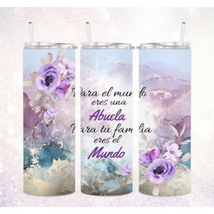 May include: A stainless steel tumbler with a watercolor background in shades of purple and blue. The tumbler features a floral design with purple flowers and green leaves. The text on the tumbler reads "Para el mundo eres una Abuela Para tu familia eres el Mundo".