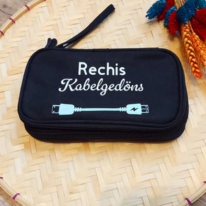 Könnte beinhalten: Schwarze Reißverschlusstasche mit einer weißen Aufschrift "Rechis Kabelgedöns" und einer blauen Grafik eines Kabels mit einem Blitz.