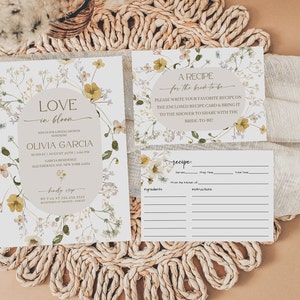 K&ouml;nnte beinhalten: Eine florale Einladung zu einer Bridal Shower mit hellbraunem Hintergrund und einem wei&szlig;en Oval mit dem Text "LOVE in bloom" und dem Namen der Braut, Olivia Garcia. Die Einladung enth&auml;lt Datum, Uhrzeit und Ort der Shower. Eine Rezeptkarte mit floralem Design und dem Text "A RECIPE for the bride-to-be" ist enthalten. Die Karte bietet Platz f&uuml;r G&auml;ste, um ihr Lieblingsrezept einzutragen.
