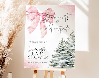 Può includere: Un cartello di benvenuto per il baby shower con un fiocco rosa e la scritta "Baby it's cold outside". Il cartello include anche la scritta "Welcome to Samantha's Baby Shower" e un'illustrazione di un albero invernale.