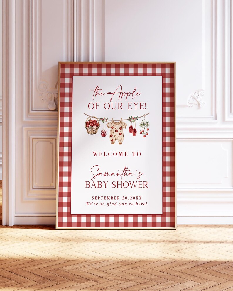Puede incluir: Un letrero enmarcado para baby shower con un borde de cuadros rojos y blancos. El letrero presenta el texto "the Apple of Our Eye!" y "Welcome to Samantha's Baby Shower." Los elementos decorativos incluyen un body de beb&eacute;, manzanas y zapatos de beb&eacute;.