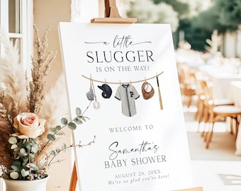 May include: A white rectangular sign on a wooden easel featuring the text A little SLUGGER IS ON THE WAY! WELCOME TO Samantha's BABY SHOWER AUGUST 20, 20XX. It displays illustrations of a baseball glove, cap, jersey, ball, and bat on a clothesline.
