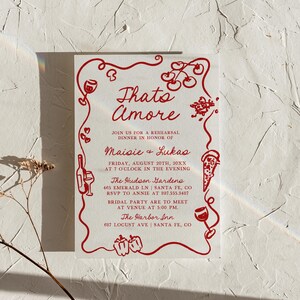 May include: Red and white invitation with a whimsical illustration of tomatoes, peppers, wine glasses, and pizza slices. The text reads "Thato Amore" and includes the names "Maisie & Lukas" for a rehearsal dinner. The event is at The Hudson Gardens on August 20th at 7:00 PM. The bridal party is to meet at The Harbor Inn at 5:00 PM.