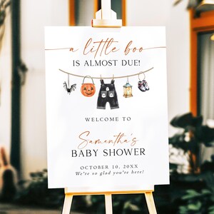 以下が含まれることがあります： A little boo IS ALMOST DUE! WELCOME TO Samantha's BABY SHOWER OCTOBER 10, 20XX We're so glad you're here! という文字と、コウモリ、カボチャ、オーバーオール、ランタン、靴が描かれた洗濯ロープのイラストが印刷された白い長方形のベビーシャワー用サインボード。