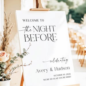 Pu&ograve; includere: Un cartello di benvenuto bianco su un cavalletto di legno. Il cartello recita "WELCOME TO The NIGHT BEFORE celebrating Avery & Hudson OCTOBER 10, 2026 WE'RE SO GLAD YOU'RE HERE!" in nero.