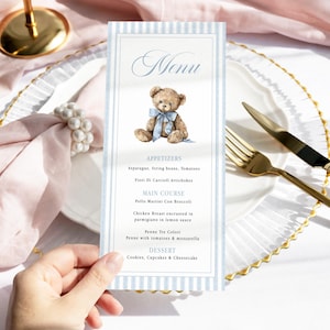 May include: A vertical rectangular menu card featuring a light blue striped border and a watercolor illustration of a brown teddy bear with a blue bow. The text reads Menu, Appetizers, Main Course, Pollo Martini Con Broccoli, and Dessert.