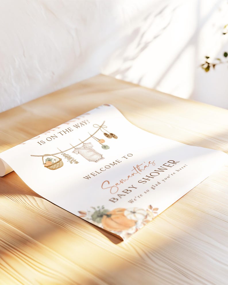 May include: A white rectangular baby shower welcome sign featuring the text IS ON THE WAY, WELCOME TO Samantha's BABY SHOWER, and We're so glad you're here. The design includes illustrations of a clothesline with baby items and pumpkins.