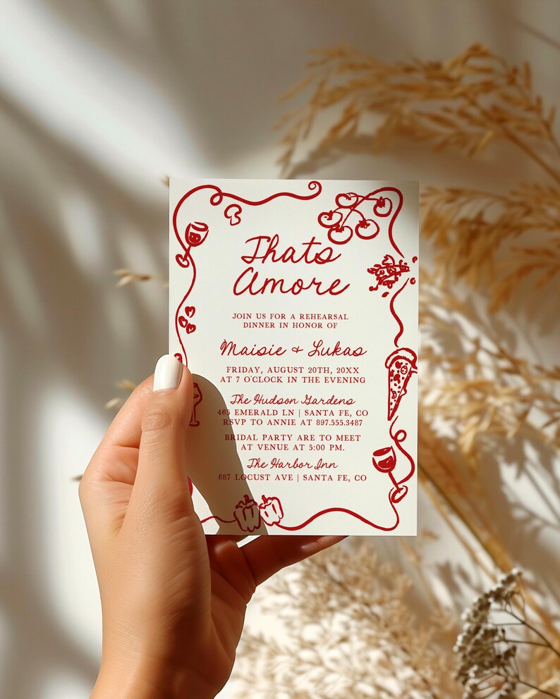 May include: A red and white invitation card with the text "Thats Amore" and details for a rehearsal dinner in honor of Maisie and Lukas. The card features a red illustration of a wine glass, cherries, and a pizza slice.