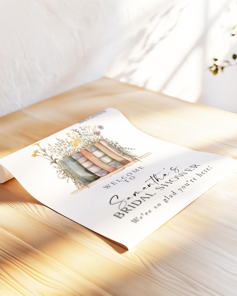 May include: A rolled-up white paper sign with the text "Welcome to Samantha's Bridal Shower". The sign features a watercolor illustration of books and flowers. The sign is on a wooden surface.