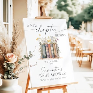 May include: A white welcome sign on a wooden easel, with the text "A New Chapter Begins" in black script. Below, a watercolor illustration of books and flowers. The sign welcomes guests to Samantha's Baby Shower.