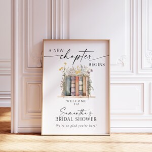May include: A framed poster with the text "A New Chapter Begins" above a watercolor illustration of books and flowers. The poster welcomes guests to Samantha's bridal shower. The poster is 18x24 inches.