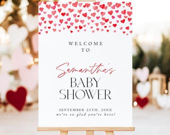 Może przedstawiać: Biała tablica powitalna na drewnianej sztaludze z obramowaniem z czerwonych i różowych akwarelowych serc u góry. Tekst brzmi: WELCOME TO Samantha's BABY SHOWER SEPTEMBER 25TH, 20XX we're so glad you're here! czarnymi i czerwonymi literami.