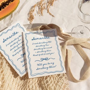 May include: Two white rectangular cards with blue wavy borders and blue cursive text that reads: Samantha, I need something old, something new, something borrowed, something blue, most of all I need you! Will you be my something blue?
